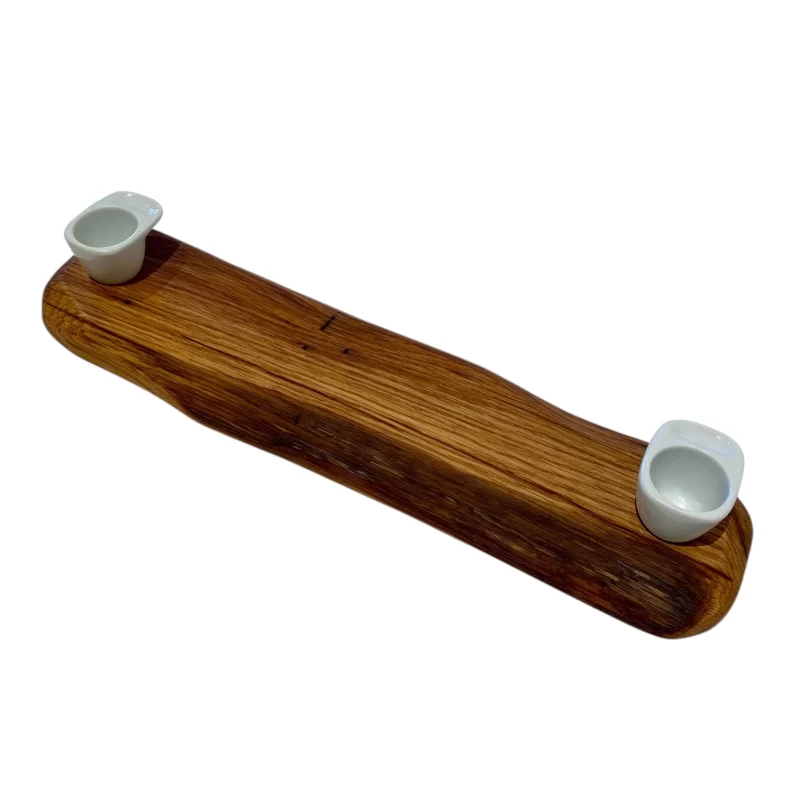 Handcrafted, long and narrow rectangular wooden cutting board with an irregular edge and two white ceramic bowls for jams, sauces or coffee.