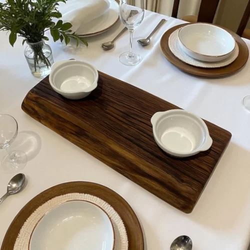 Tagliere artigianale in legno rettangolare stretto e lungo con bordo irregolare e due ciotole in ceramica bianca per marmellate, salse o caffè.